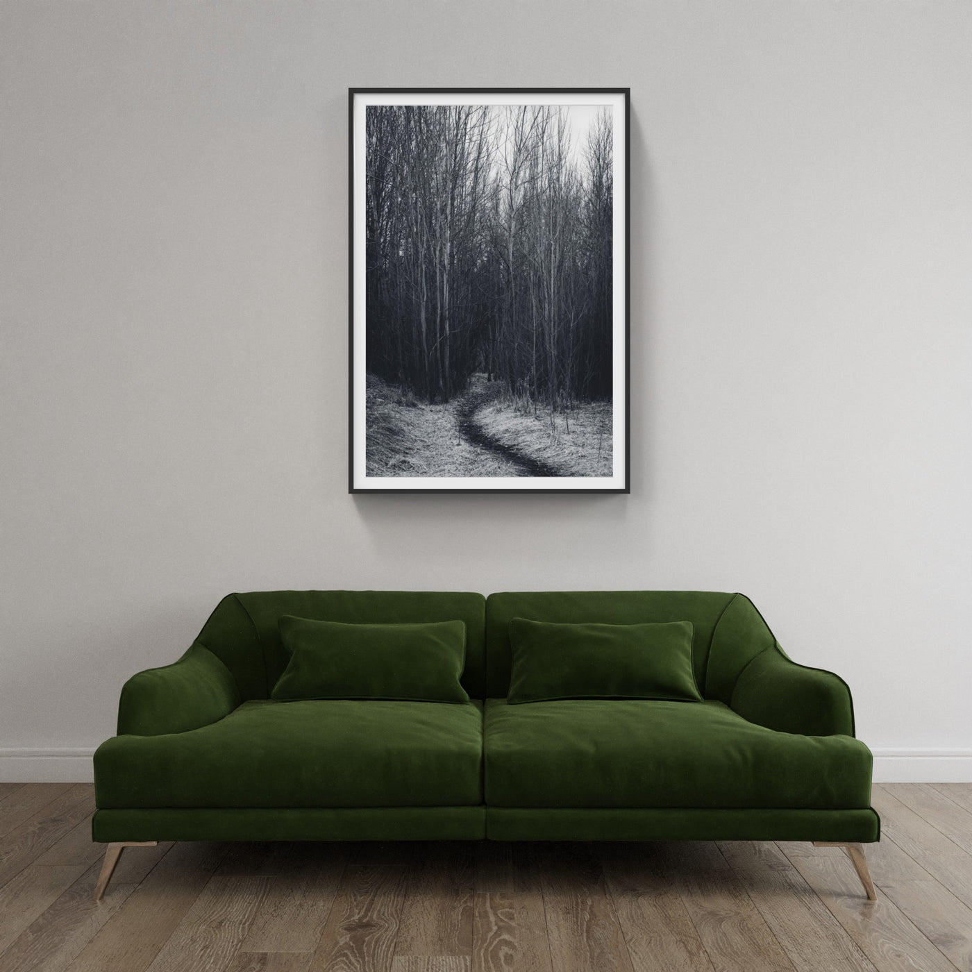 Dark narrow wooded forest with a path photo hanging above a green couch
